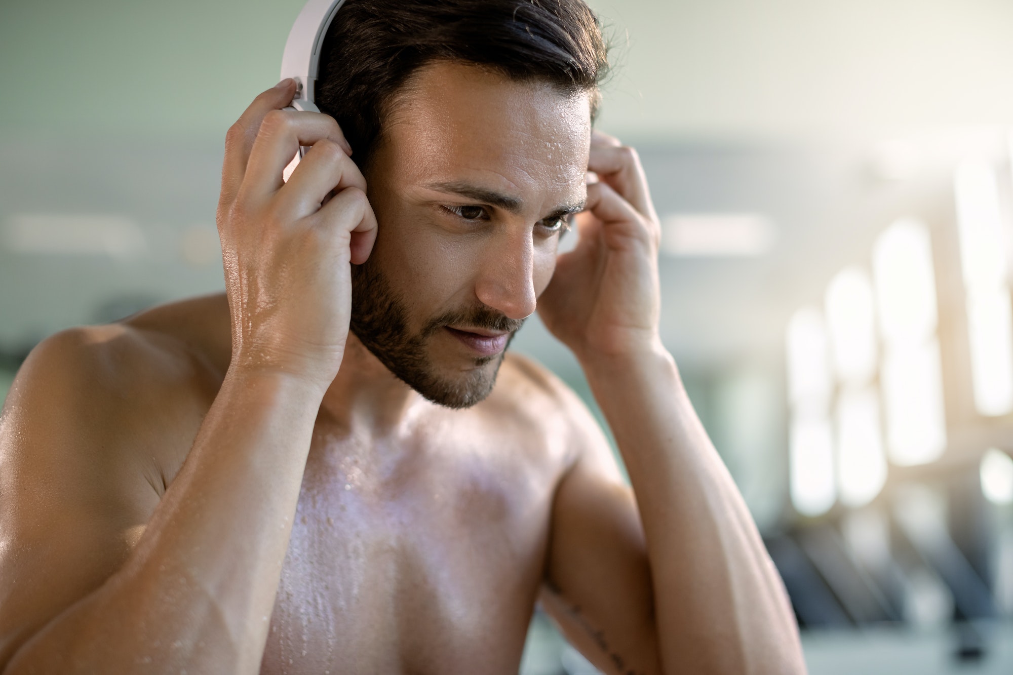 Sweaty athlete listening music over headphones in health club.